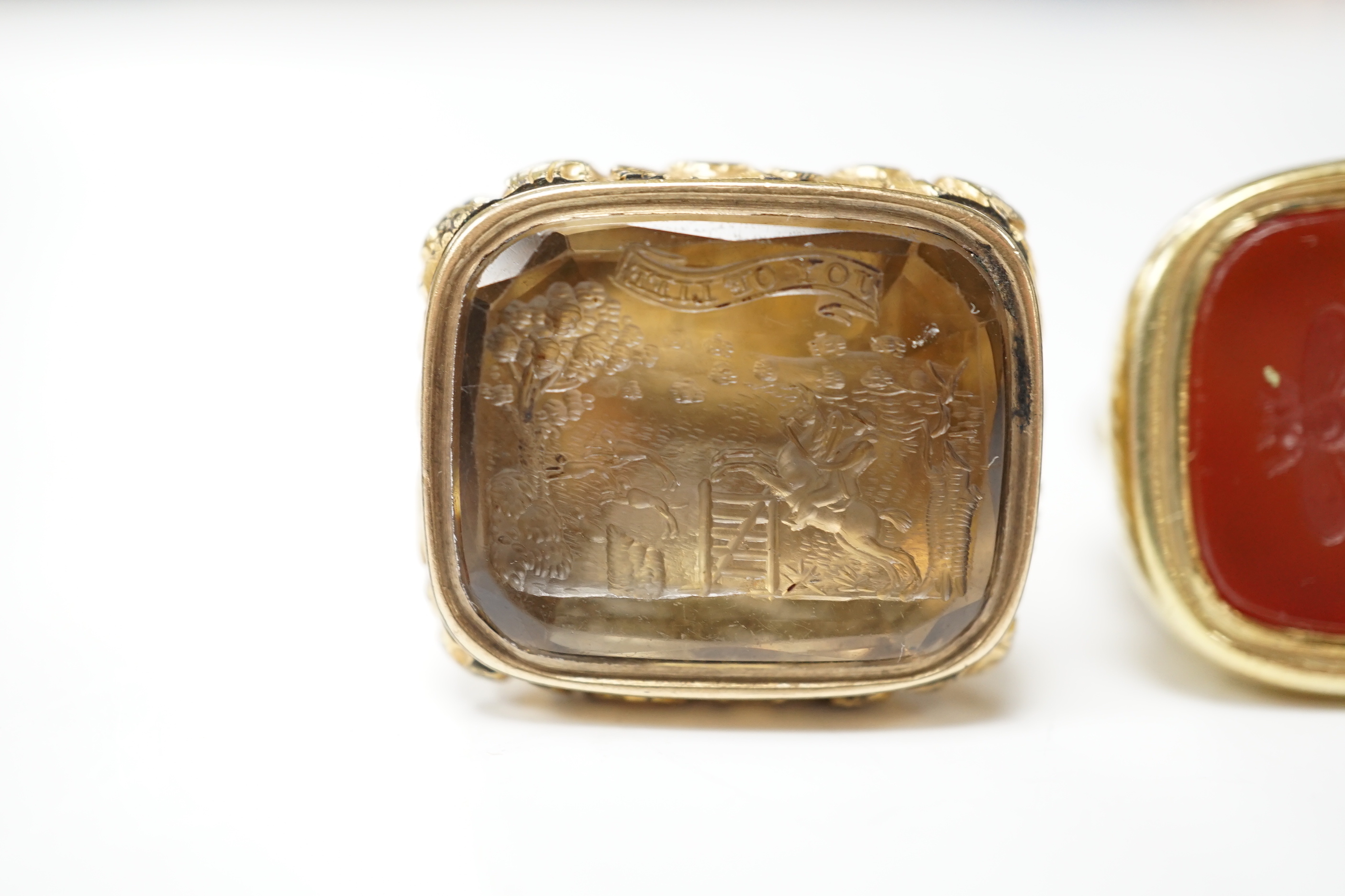 Two 19th century yellow metal overlaid fob seals, the largest 32mm with inset citrine carved with ornate crest and inscribed 'Joy of Life', the other with inset carnelian craved with bee and inscribed 'Non Sibi'.